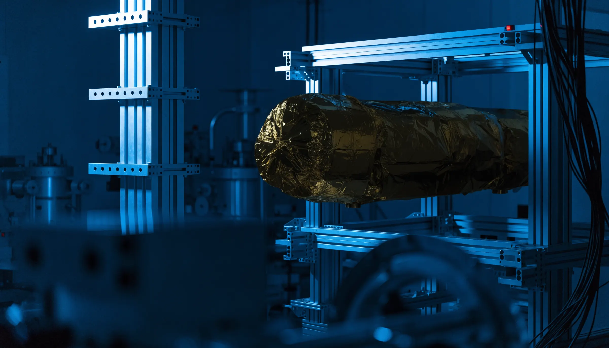 Spacecraft wrapped in gold multi-layer insulation under assembly in a dim cleanroom